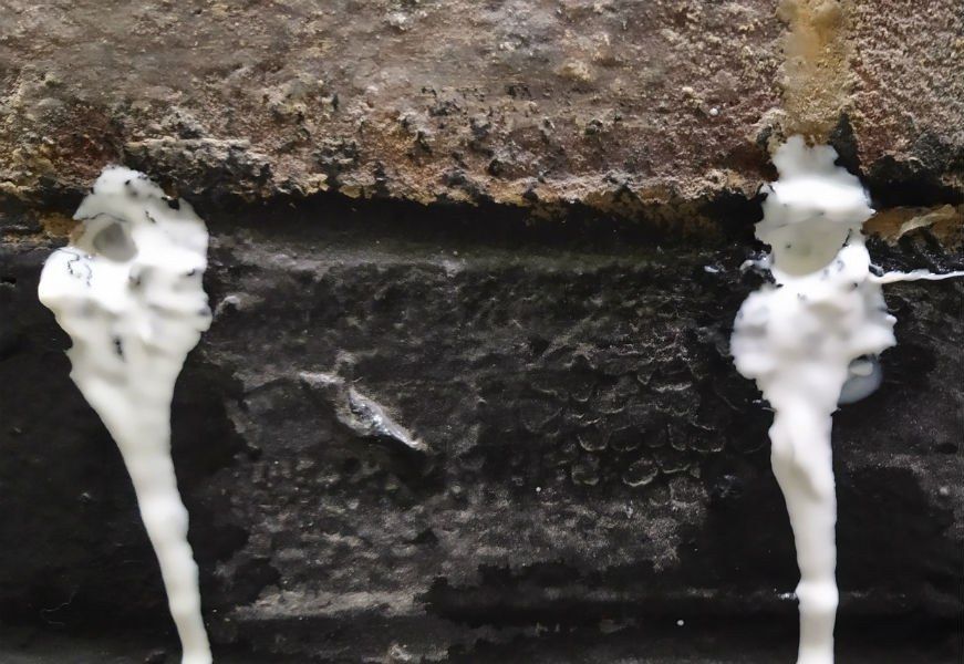 Crème d'injection blanche qui ressort de deux trous forés dans le joint d'un mur