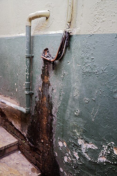 Mur abîmé par une fuite autour d'une descente d'eau, peinture décollée et traces de rouille
