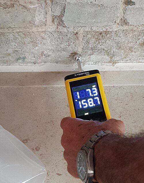 Mesure de l'humidité d'un mur en blocs avec un humidimètre électronique tenu à la main