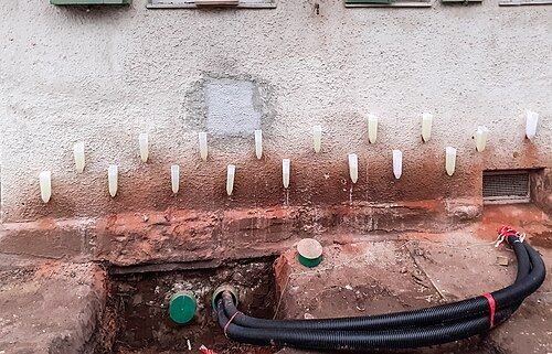 Injection par gravité : rangée d'entonnoirs insérés dans le pied d'un mur enduit