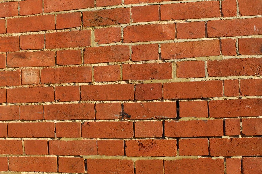 Mur de briques rouges aux joints creusés et abîmés, par où la pluie peut s'infiltrer