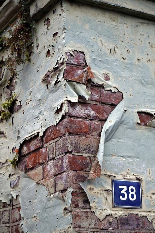 Peinture qui cloque et s'écaille sur un mur, laissant apparaître les briques
