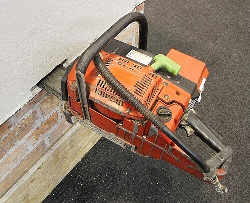 Tronçonneuse à chaîne utilisée pour scier un mur de briques en pied de mur